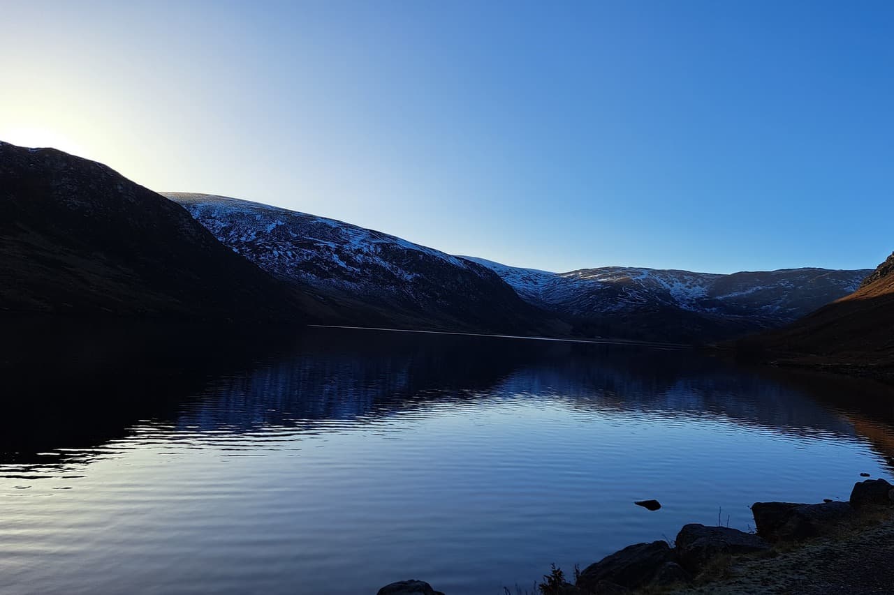 A serene day at Loch Lee in Glenesk, where the still waters reflect the surrounding mountains beneath a clear blue sky.
